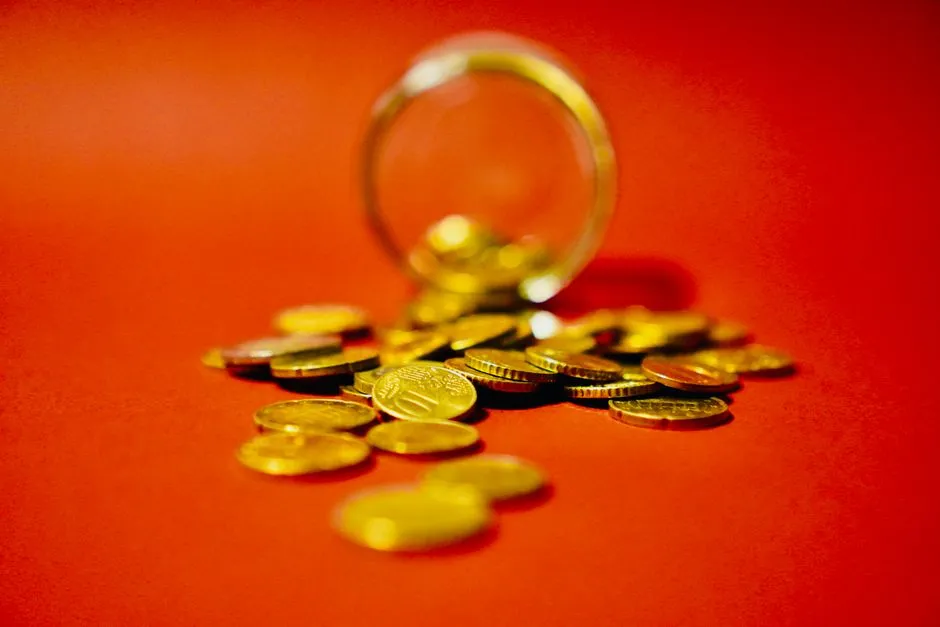 Gold-coloured coins spilling from a glass jar on a red background, illustrating a report on MariBank's regional expansion.