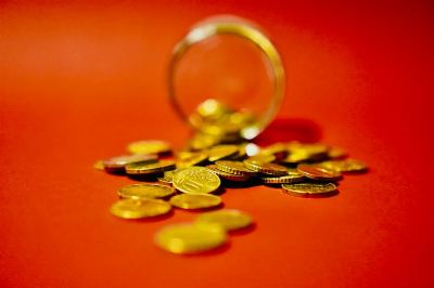 A collection of golden coins spilling from a glass jar on a vibrant red background symbolizes wealth.