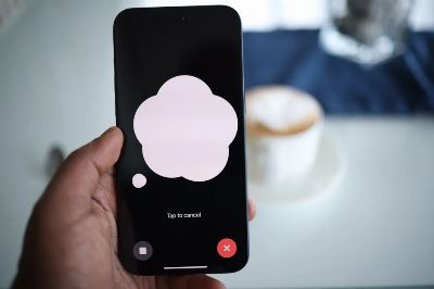 Close-up of a smartphone in hand with AI voice chat bubble and coffee in background.