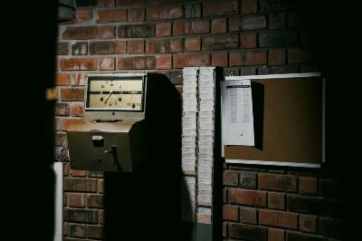 A retro time clock and stack of punch cards against a dark brick wall in an industrial setting.