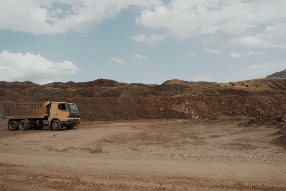A heavy haul truck on a dirt road at an open-cast mine, with excavated ground and a pale sky behind it.