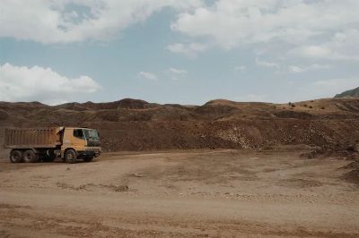 A solitary dump truck at a quarry site under a cloudy sky.