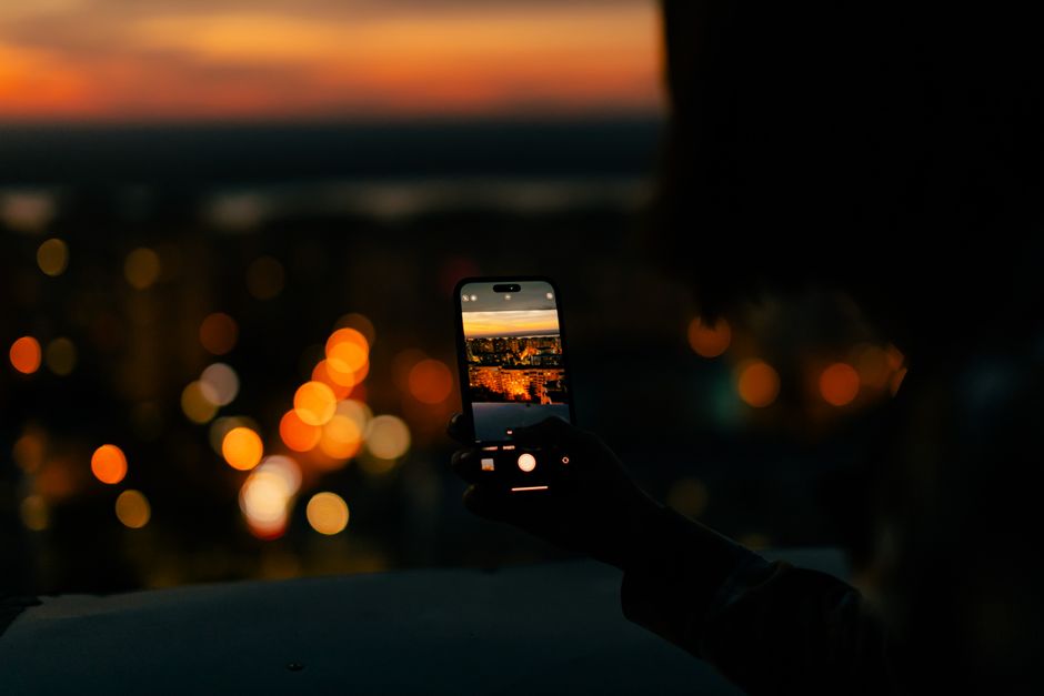 A person photographing a cityscape with a smartphone during sunset, showcasing vibrant city lights.