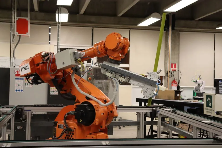 An orange industrial robot arm holding a metal fixture in an engineering laboratory, illustrating a report on funding for robot training simulation.