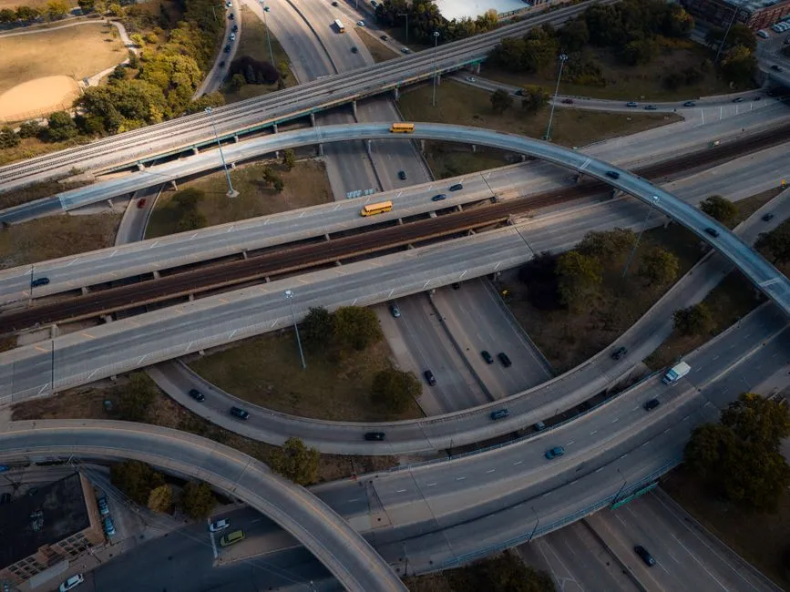 An aerial view of a multi-level motorway interchange carrying light traffic, with trees between the ramps.