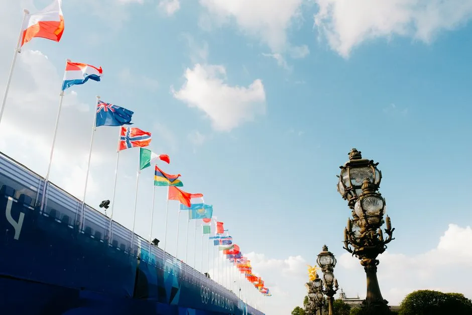 Colorful flags waving against a blue sky next to ornate lamp posts in Paris, France.
