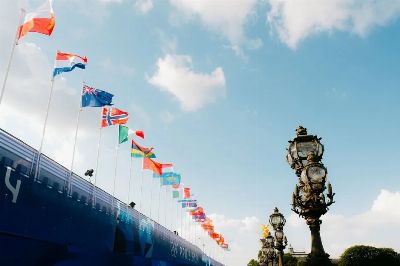 Colorful flags waving against a blue sky next to ornate lamp posts in Paris, France.