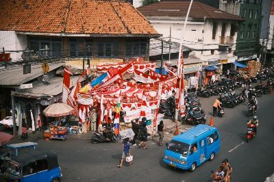 Colorful street market scene in Jakarta, Indonesia, displaying red and white flags amidst busy traffic.