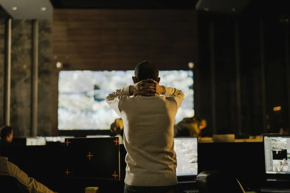 A person seen from behind standing before a wall of monitors in a dim operations room, illustrating a report on monitoring requirements imposed on a frontier AI model.