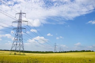 Power pylons in a green field under a bright blue sky in England.