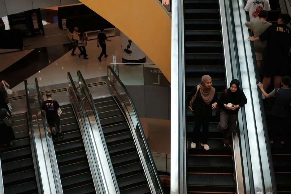 Shoppers riding escalators between floors of a shopping mall, seen from above
