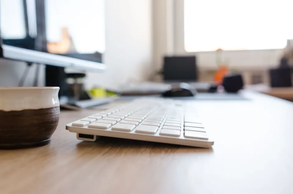 A keyboard and coffee cup on an office desk with a monitor out of focus behind, illustrating a report on an exploited flaw in Zimbra Collaboration mail servers.