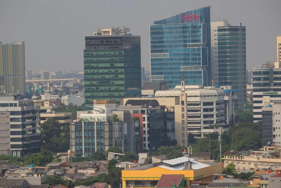 Jakarta office towers rising through daytime haze above low-rise rooftops