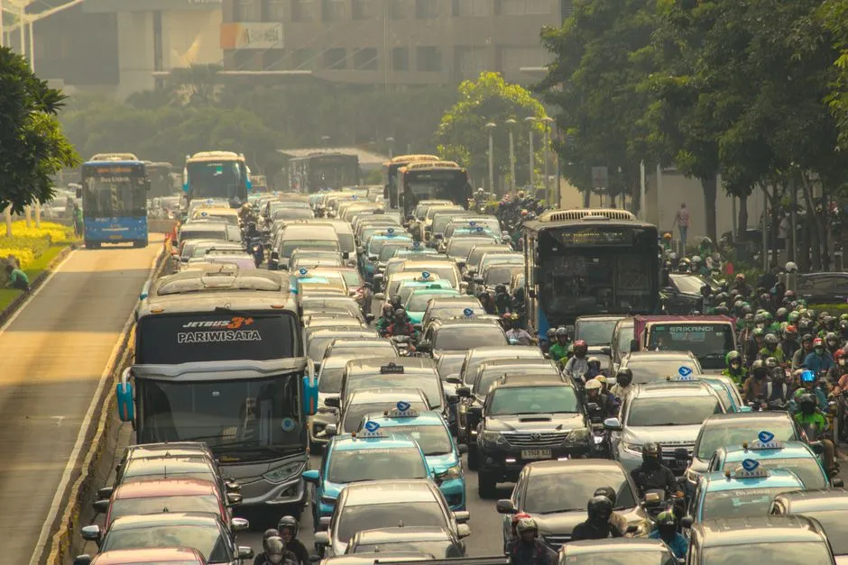 Dense Jakarta traffic in haze, with motorbike riders packed between city buses and taxis on a multi-lane road
