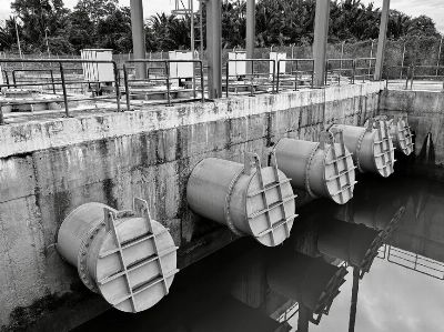 Monochrome image of large industrial water pipes with valves.