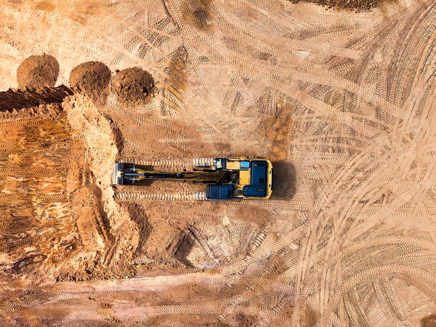 An excavator seen from directly above, working bare earth marked with track lines