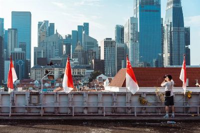 A photographer takes a picture of the Singapore skyline under a clear blue sky.