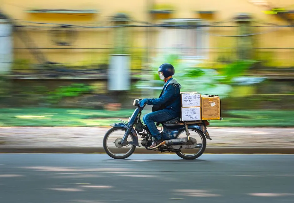 A helmeted delivery rider carrying parcels on a motorbike, panned against a blurred street, illustrating a report on a Southeast Asian commerce and lending group.
