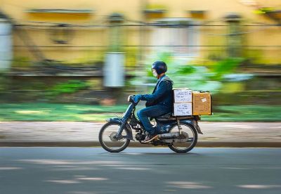 Side view of a motorcycle courier speeding down a road with packages in motion blur background.