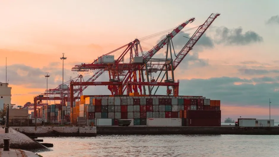 Container cranes and stacked shipping containers at a port under a pink sunset sky, illustrating a report on restricted AI accelerator shipments reaching China.