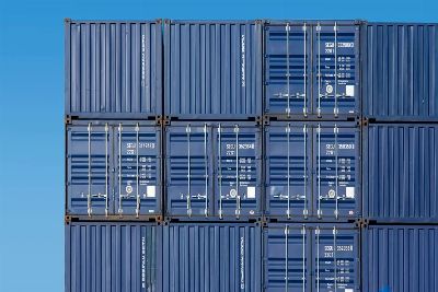 Close-up of blue shipping containers stacked high at Rotterdam Port under a clear blue sky.