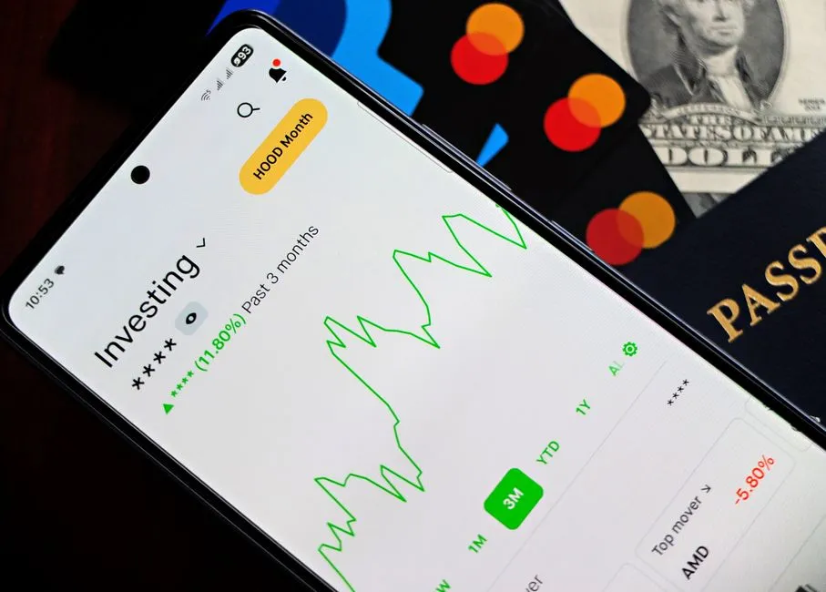 A smartphone showing an investment app with green growth indicators, beside credit cards, US dollars and a passport.