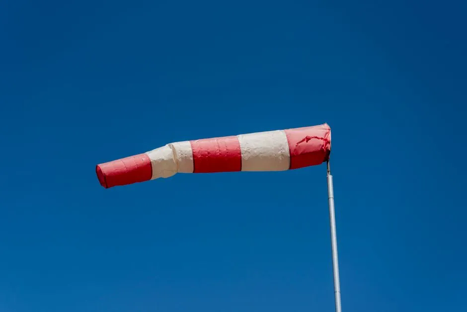 A red and white windsock held out straight by the wind against a blue sky