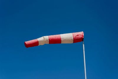 Vibrant red and white windsock blown by the wind against a clear blue sky.