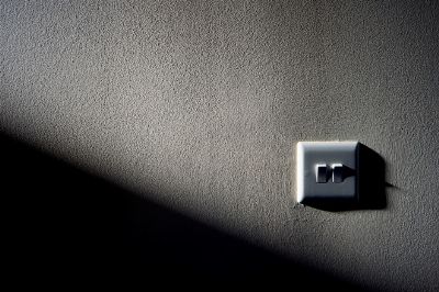 A light switch on a textured wall with contrasting shadow and light, creating a minimalist aesthetic.