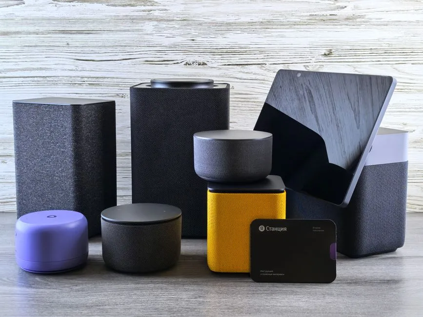 A group of smart speakers and home hub devices arranged on a wooden surface