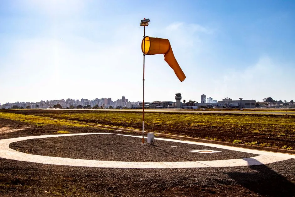 An orange windsock on a pole, filled by the wind, beside an airfield
