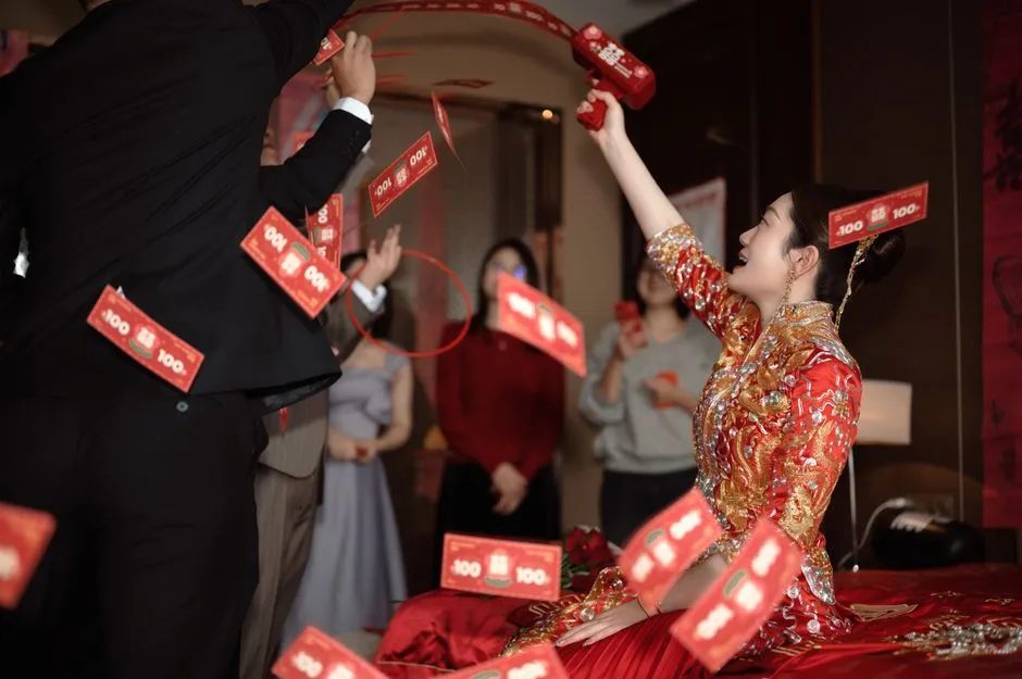 A bride in a red and gold wedding dress laughing as red envelopes fly around her