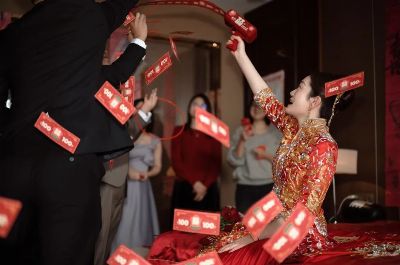 Chinese wedding celebration with bride in traditional attire as red envelopes fly through the air.