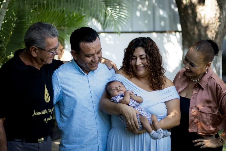 Several generations of one family standing together outdoors around a baby