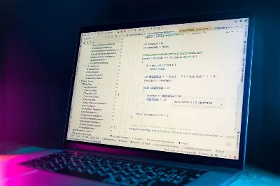 A laptop screen showing a code editor with visible programming code in a dimly lit environment.