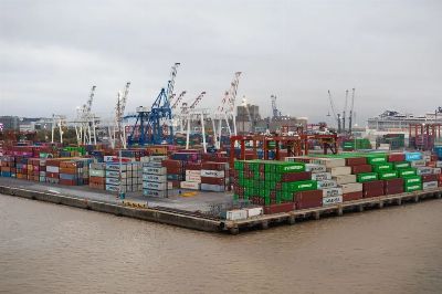 A bustling shipping port with stacked cargo containers and cranes under overcast skies.