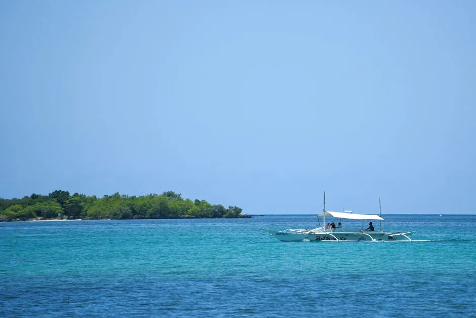 A traditional outrigger boat on turquoise water with a small forested island behind, illustrating a report on a proposed Philippine domestic submarine cable network.