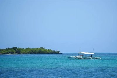 Scenic view of a traditional boat sailing near lush green islands in Central Visayas, Philippines.
