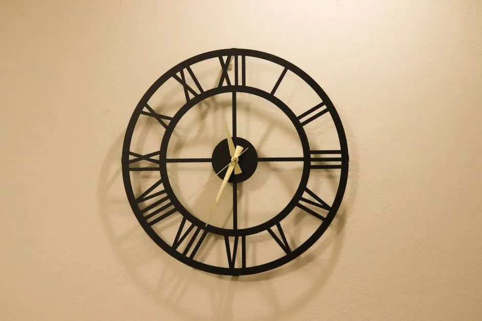 A black metal wall clock with Roman numerals and gold hands on a cream wall