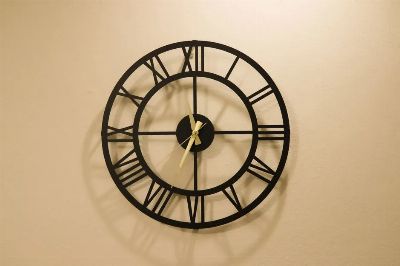 Decorative black metal wall clock with Roman numerals on a beige wall, creating a classic look.
