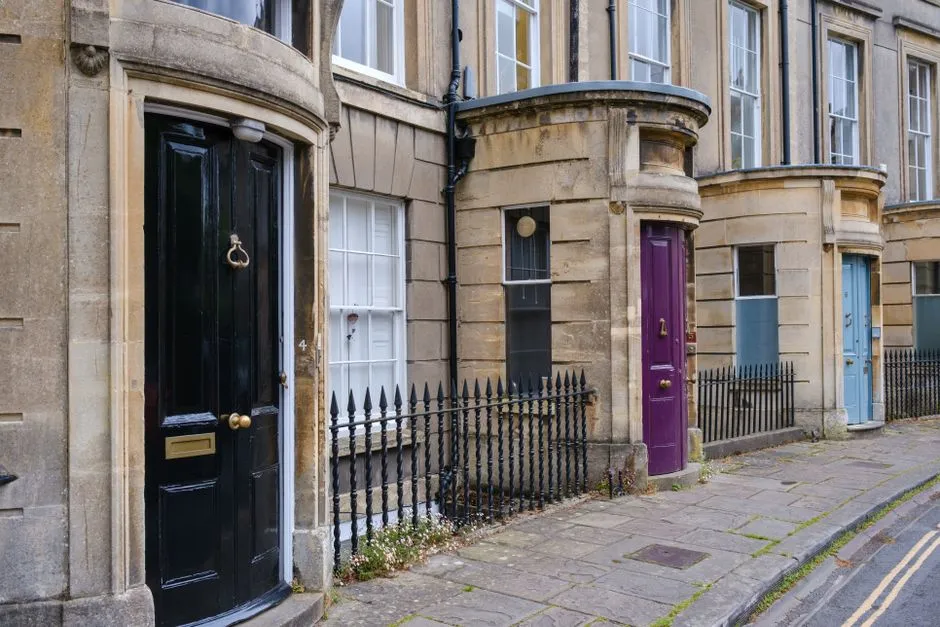 A row of terraced front doors along a stone street, one of them painted a bright purple that stands out from its neighbours