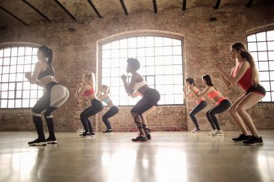Women participating in a group fitness class performing squats in an industrial-style studio.