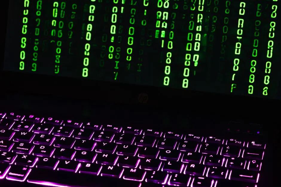 Green code cascades down a laptop screen above a backlit keyboard