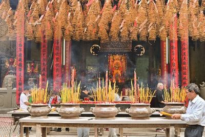 A bustling Chinese temple with incense and worshipers in an atmospheric setting.