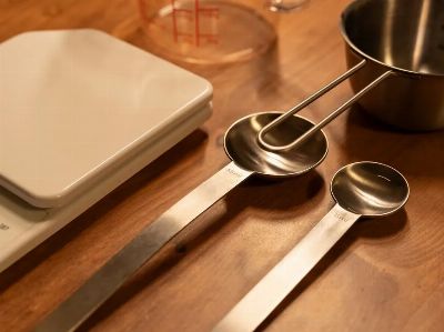 A close-up of kitchen utensils including a scale, measuring cups, and spoons on a wooden counter.