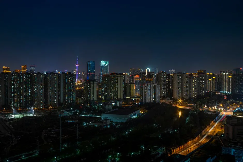A dense city skyline lit up at night, with a broadcast tower rising among high-rise blocks.