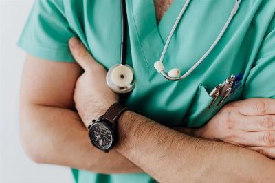 Unrecognizable man wearing medical uniform with stethoscope and pens standing in hospital with crossed arms during work in d…