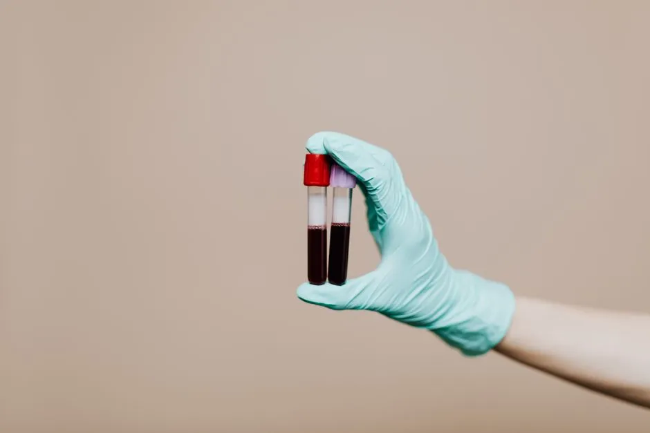 A gloved hand holding two blood sample tubes against a plain background