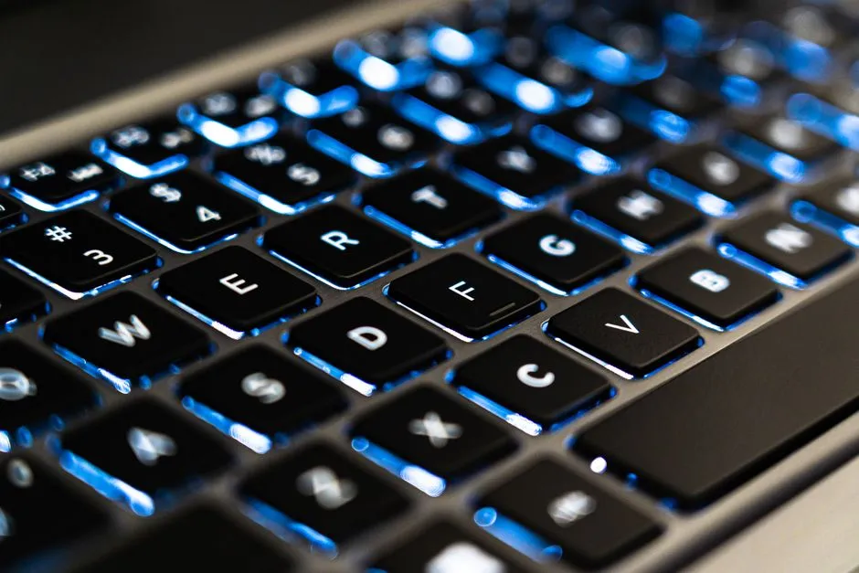 A close-up of a laptop keyboard, the keys backlit in blue.