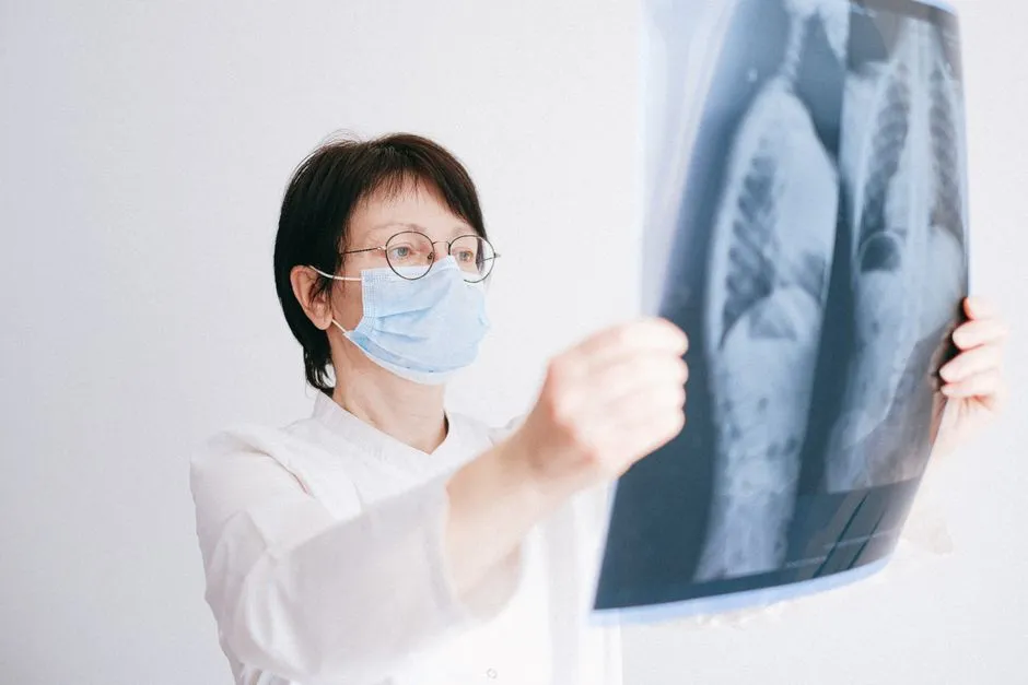 A clinician in a mask holding a chest X-ray film up to the light